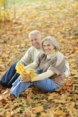 Beautiful senior couple sitting on grass with leaves