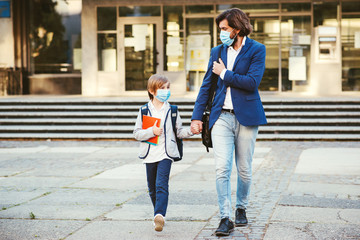 Back to school during coronavirus pandemic. Father taking son to school. Dad and schoolboy wearing face masks.