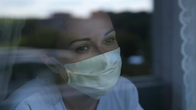 Young woman wears a mask to protect herself from covid-19 while looking out the window