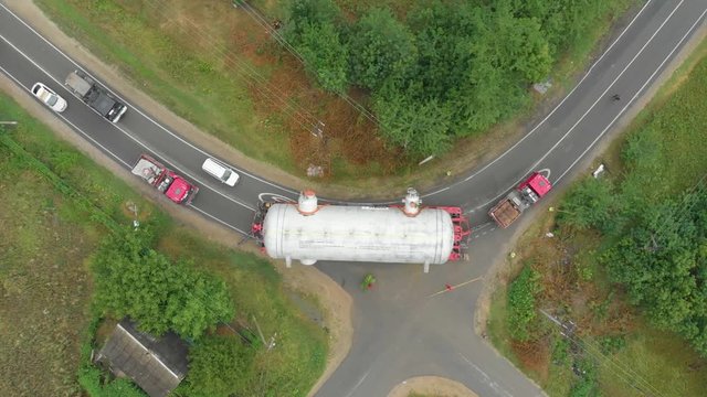 A truck driver with an oversized cargo on a trailer makes a turn on a narrow road followed by a traffic inspection vehicle. Delivery and logistics of goods from different places, top view