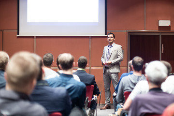 Speaker giving a talk in conference hall at business meeting event. Rear view of unrecognizable people in audience at the conference hall. Business and entrepreneurship concept.