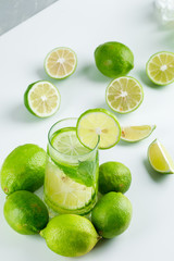 Fototapeta na wymiar Lemonade in a glass with lemons, herbs high angle view on white and grey background