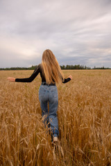 A girl with long blond hair walks across a rye field.