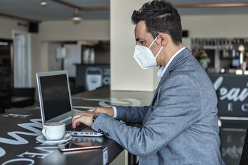 Businessman in protective mask using laptop in cafe