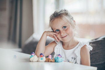 Little cute preschooler child girl playing educational games with plasticine figures preparing for school in kindergarten while sitting at table. Back to school concept.