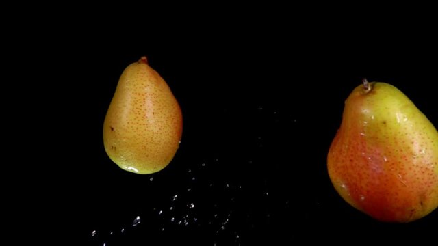 Two red ripe pears are flying towards each other and colliding on a black background in slow motion
