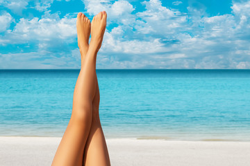 Beautiful long crossed outstretched female tanned legs against the background of the ocean,...