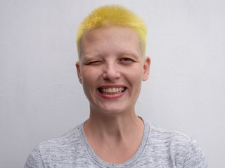 Middle aged woman with yellow-green hair laughs on white background, showing perfect white teeth, grimaces and gestures in front of camera