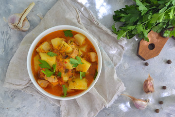 Vegetable stew in a white bowl. Light background. Linen cloth. Stew with potatoes, chicken, carrots and herbs. Top view