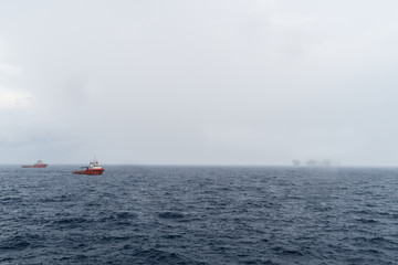 Misty morning at oil filed with anchor handling tugboat and oil production platform complex in the background