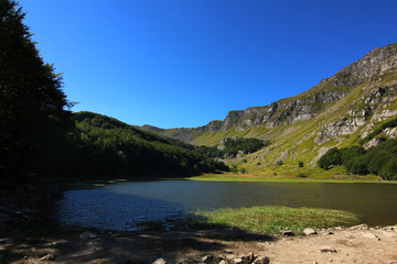 Paesaggio estivo di montagna nell’Appennino modenese; veduta tra sentieri, boschi di faggio, rocce e un piccolo lago