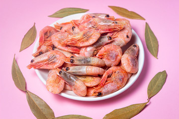 Shrimps on a white plate. Boiled shrimp in a plate on a pink background. Laurel leaves lie around
