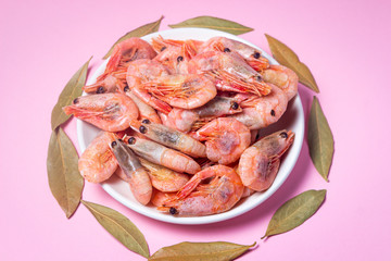 Shrimps on a white plate. Boiled shrimp in a plate on a pink background. Laurel leaves lie around