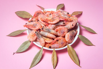 Shrimps on a white plate. Boiled shrimp in a plate on a pink background. Laurel leaves lie around