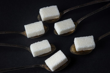 Sugar on a black background. Spoons with sugar cubes. The spoons lie next to each other