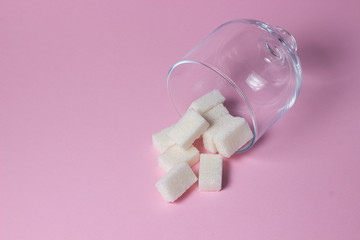 Sugar cubes on a pink background. Sugarcubes spilled out of glassware