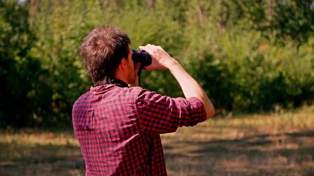 Man looking through binocular at the forest. Bird watching. Nature explore. Hiking tourist. 