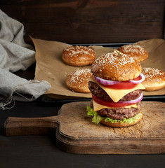 double cheeseburger with tomatoes, onions, barbecue cutlet and sesame bun on an old wooden cutting board