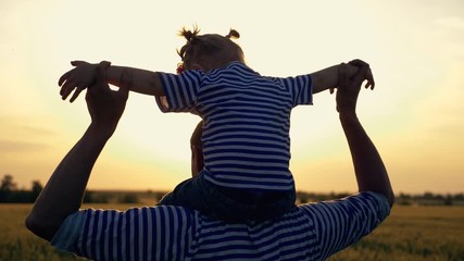Happy family in the field on a walk in the sunset. The child is sitting on the shoulders of a caring father. Dad plays with his favorite daughter.