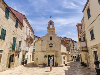 Female tourist taking photo of mall church on square of small urban village of Stari grad on Hvar...