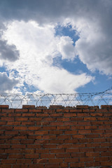 brick wall with barbed wire, with blue sky on background