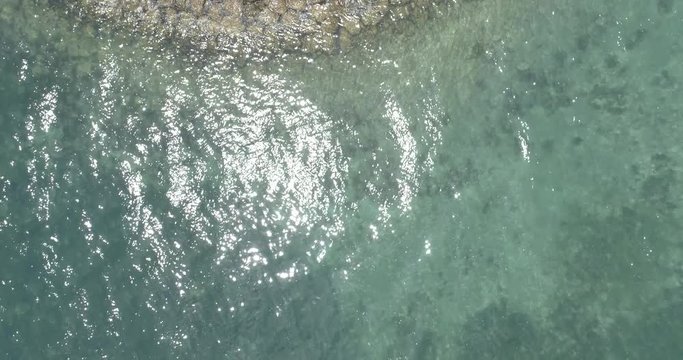 Drone shot ascending over man-made lands strip on coral reef, water sparkling in bright sunlight