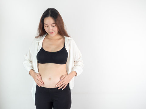 portrait of 4 months pregnant Asian woman in white bed room, Woman touching her abdomen belly on white background.