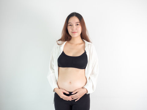 portrait of 4 months pregnant Asian woman in white bed room, Woman touching her abdomen belly on white background.