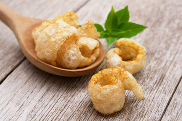 Fried pork snack ( pork rind, pork cracking ) with basil green leaf isolated on wood table background.