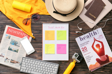 Notebook with check-list of things to pack for travel on wooden background