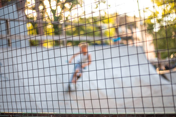 playground with slides behind a mesh fence. Boys ride skateboards and scooters, blurred background