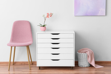 Modern chest of drawers with chair near light wall in room
