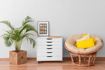 Modern chest of drawers with houseplant and armchair near light wall in room