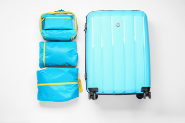 Suitcase and set of travel organizers with belongings on white background