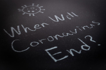 Close up of the phrase When Will Coronavirus End? by handwriting by white coloured chalk on blackboard. The surface of blackboard is powdery and rough.