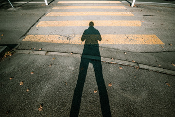 Shadow of man standing on road and crosswalk