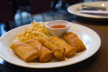 Crunchy Asian appetizer - deep fried spring rolls stuffed with vegetables and served with coleslaw salad and hot chili sauce