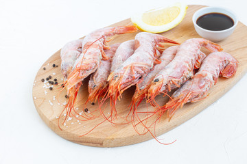 Frozen langoustines (big shrimps), lemon and spices on wooden board. Ingredients for cooking seafood