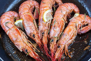 Fried big shrimps (Langoustine) with rosemary and lemon in frying pan. Seafood