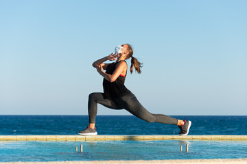 Young woman with protective surgical face mask performing yoga stretching exercises outdoor during...