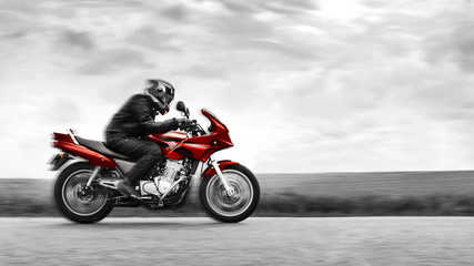 Fototapeta na wymiar A biker rides a red motorcycle at high speed. Black and white. Selective color effect