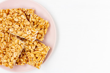 Plate of peanut brittle candy pieces in a pink plate on a white wooden background. Top view, copy space