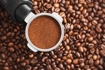Against the background of fragrant roasted natural grains is a holder from the coffee maker, in the filter of which ground coffee is rammed, which will make a strong espresso. The view from the top.
