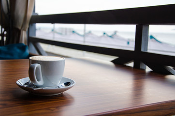White cup of cappuccino on wooden table in cafe