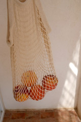 Reusable mesh bag with peaches, illuminated by sunlight. Selective focus.