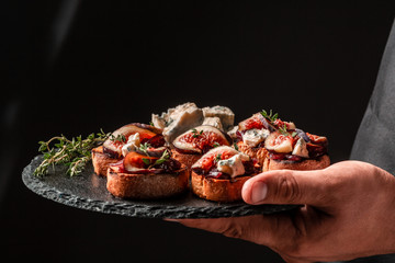 Canape or crostini with toasted baguette, blue cheese, onion jam, figs and fresh thyme on a slate board in the hands of the chef, Food recipe background. space for text