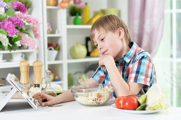 Cute little boy preparing salad and using tablet
