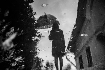 Silhouette of young girll with lace parasol reflected in puddle
