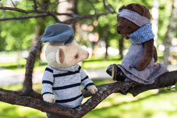 Decorative vintage dolls of a mouse and a bear sit on a tree branch in the park