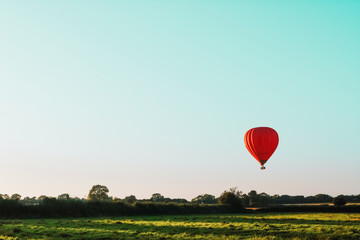 Red hot air balloon travelling over a field in the countryside during a sunset